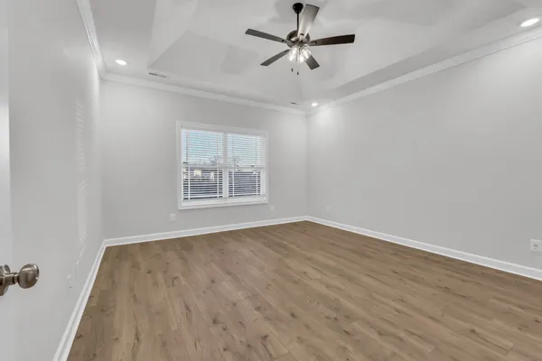 an empty room with wooden floor ceiling fan and windows