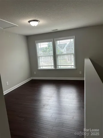an empty room with wooden floor and windows with curtains