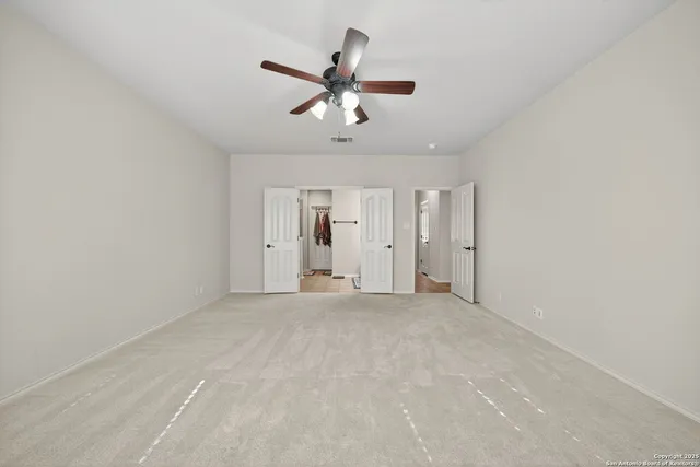 an empty room with chandelier fan and windows