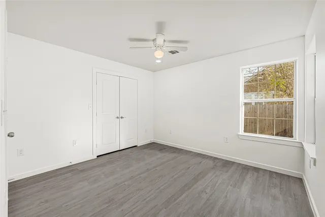 an empty room with wooden floor chandelier fan and windows