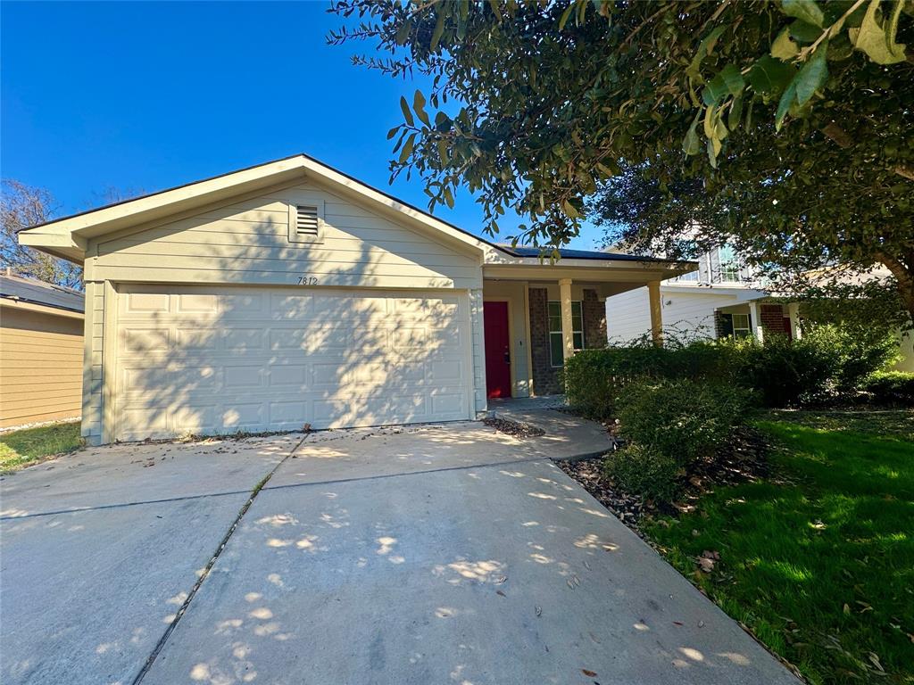 Single-story residence featuring a two-car garage, a covered entry with a red door, and a concrete driveway