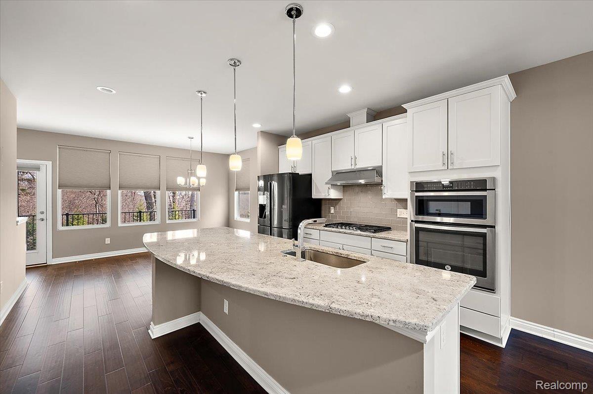 2877 Hartwick Drive Rochester, MI 48307 - Photo 16 of 44 Kitchen featuring backsplash, a center island with sink, white cabinetry, stainless steel appliances, and light stone countertops