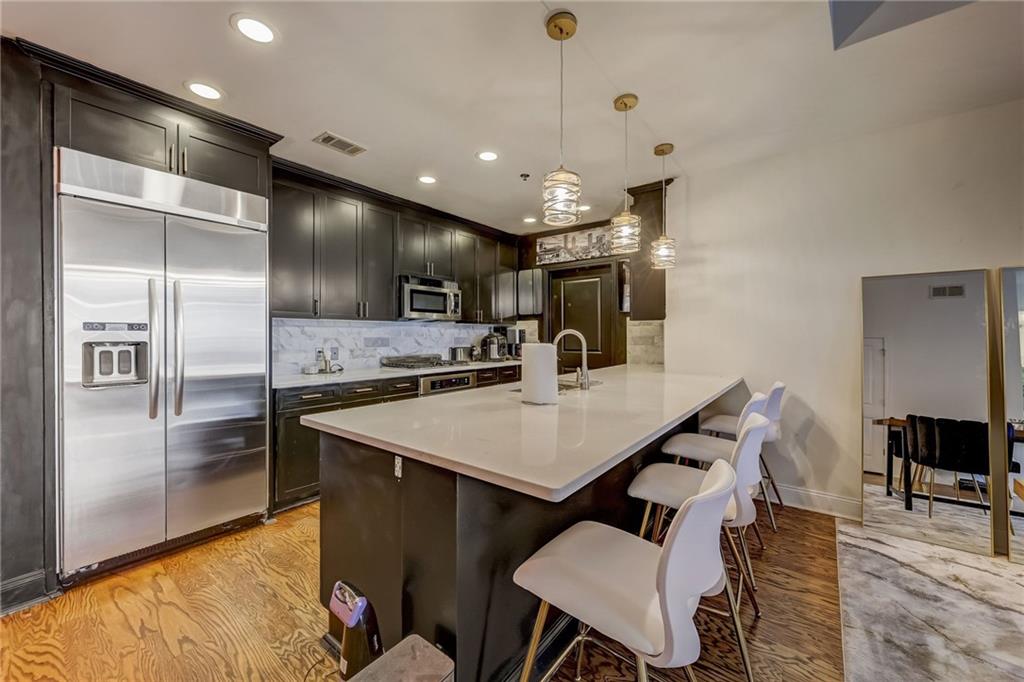 a kitchen with stainless steel appliances kitchen island granite countertop a refrigerator a stove a sink a dining table and chairs with wooden floor