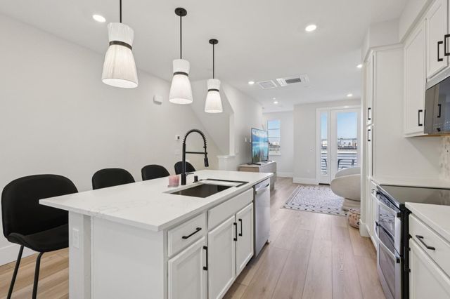 a kitchen with stainless steel appliances a stove a sink and white cabinets with wooden floor