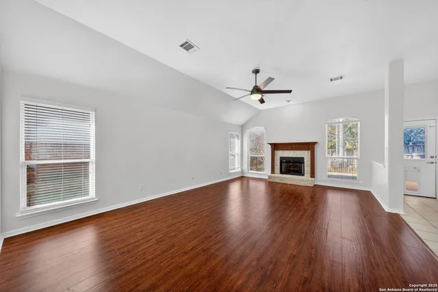 an empty room with wooden floor fireplace and windows