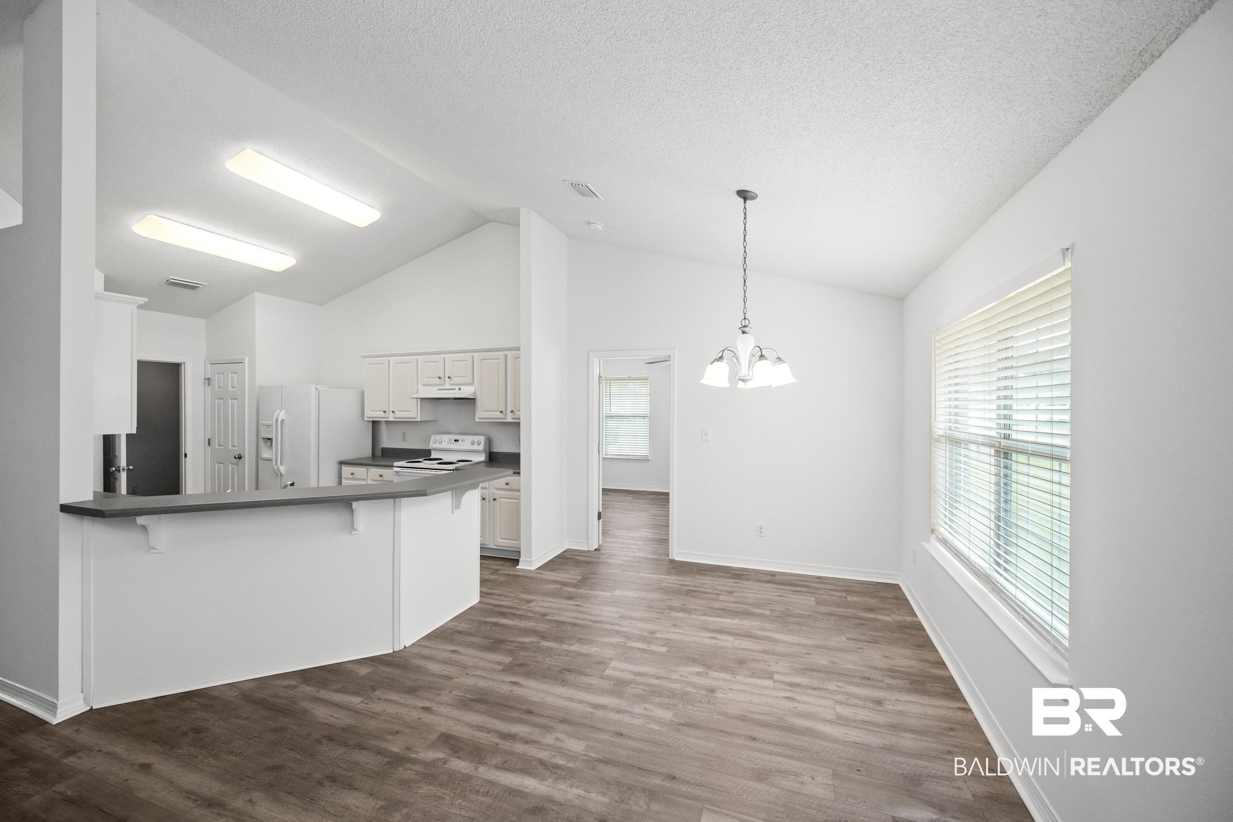 306 Monteith Oaks Drive Foley, AL 36535 - Photo 8 of 38 Kitchen with dark countertops, white appliances, a breakfast bar area, dark wood-type flooring, and high vaulted ceiling