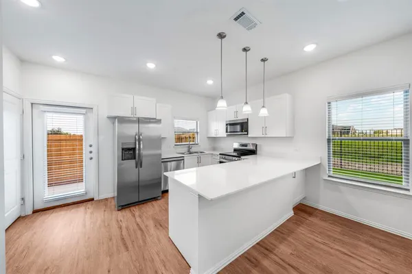 a kitchen with stainless steel appliances kitchen island granite countertop a refrigerator a sink dishwasher a oven and a dining table with wooden floor