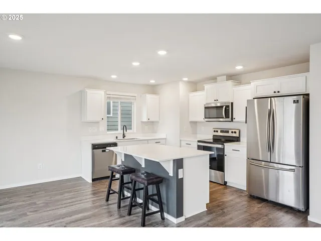 a kitchen with stainless steel appliances a refrigerator a stove a sink dishwasher a dining table and chairs with wooden floor