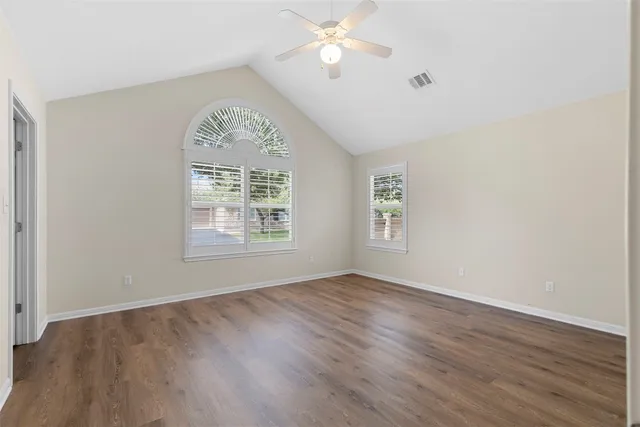 an empty room with wooden floor chandelier fan and windows