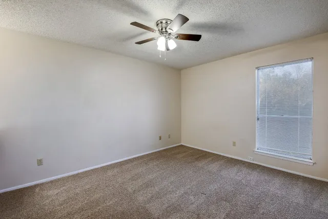 an empty room with chandelier fan and windows