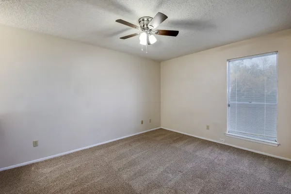 an empty room with chandelier fan and windows