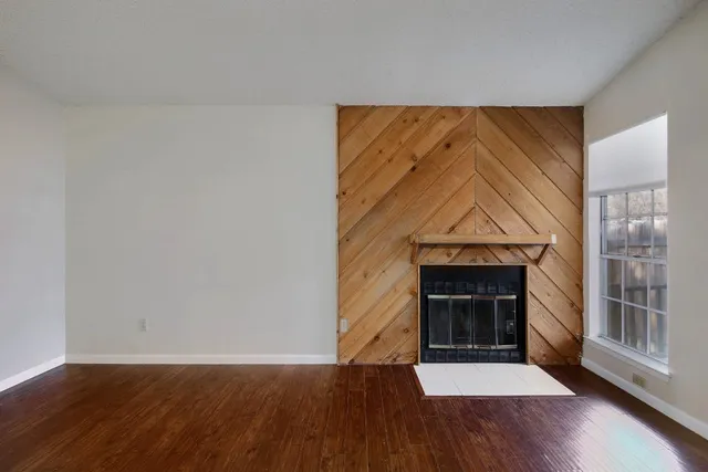 a view of an empty room with wooden floor fireplace and a window