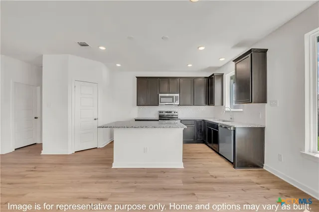 a large white kitchen with stainless steel appliances kitchen island granite countertop a stove a sink a refrigerator and a microwave