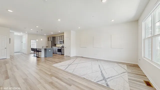 a view of an empty room with wooden floor and a kitchen