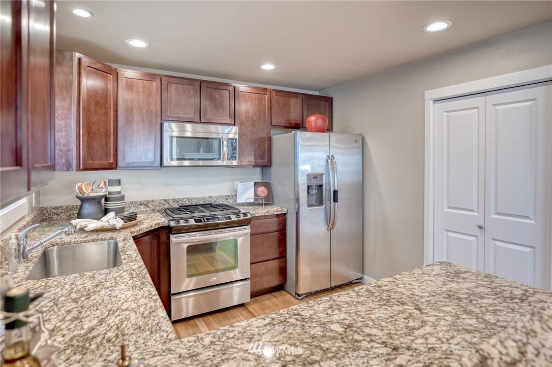 946 North 96th Street Seattle, WA 98103 - Photo 11 of 24 a kitchen with stainless steel appliances granite countertop a stove a refrigerator and a sink with wooden cabinets
