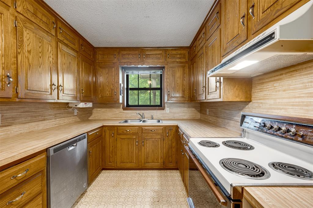 8798 Hill N Dale Road Tyler, TX 75709 - Photo 11 of 31 U-shaped kitchen featuring wood cabinetry, laminate countertops, a stainless steel dishwasher, a white electric range with overhead ventilation, and a double basin sink beneath a window