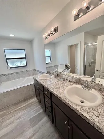 a spacious bathroom with a granite countertop double vanity sink a mirror and a bathtub