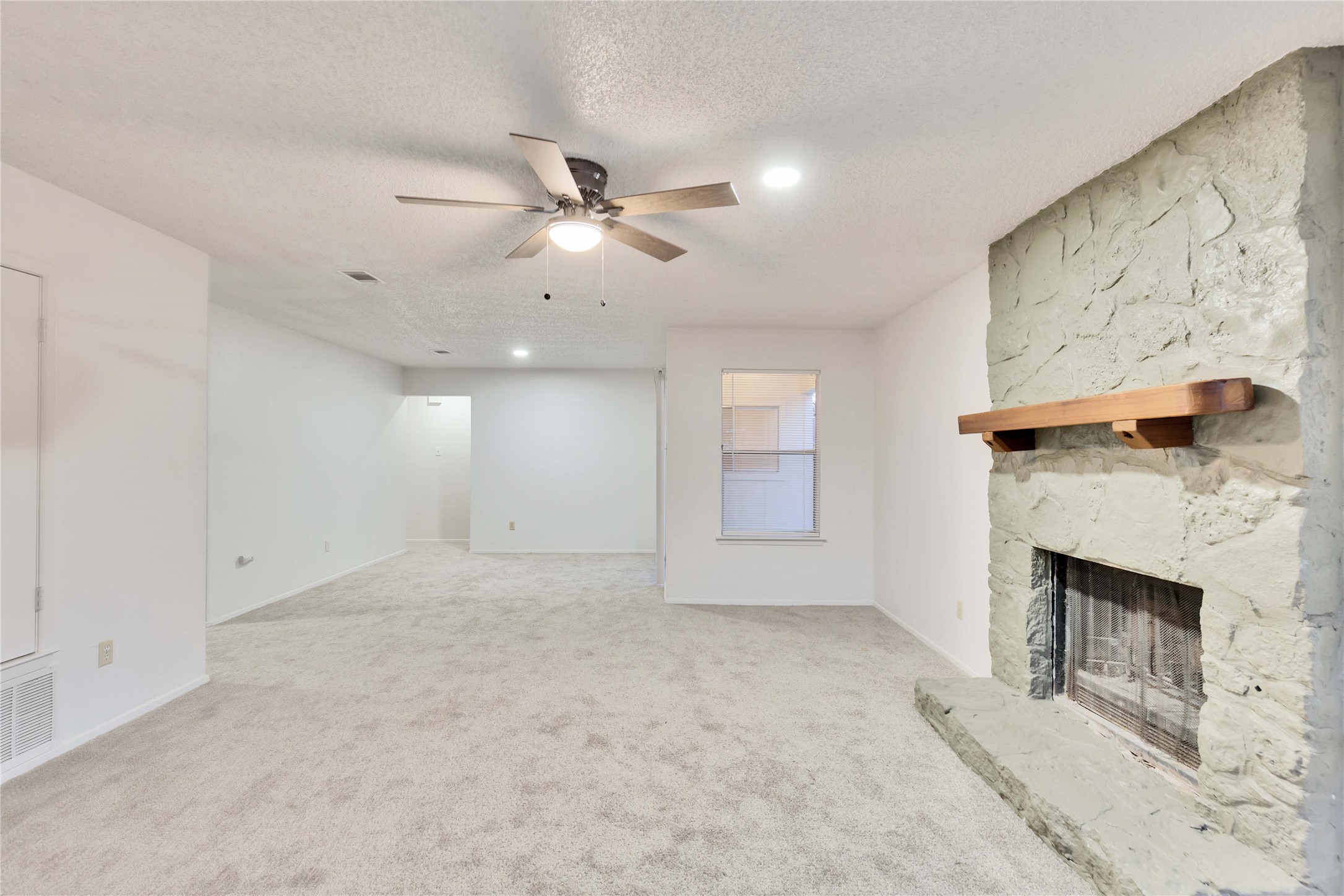 Spacious room featuring a stone fireplace with a wood mantel, light gray carpet, white walls, a ceiling fan, and recessed lighting