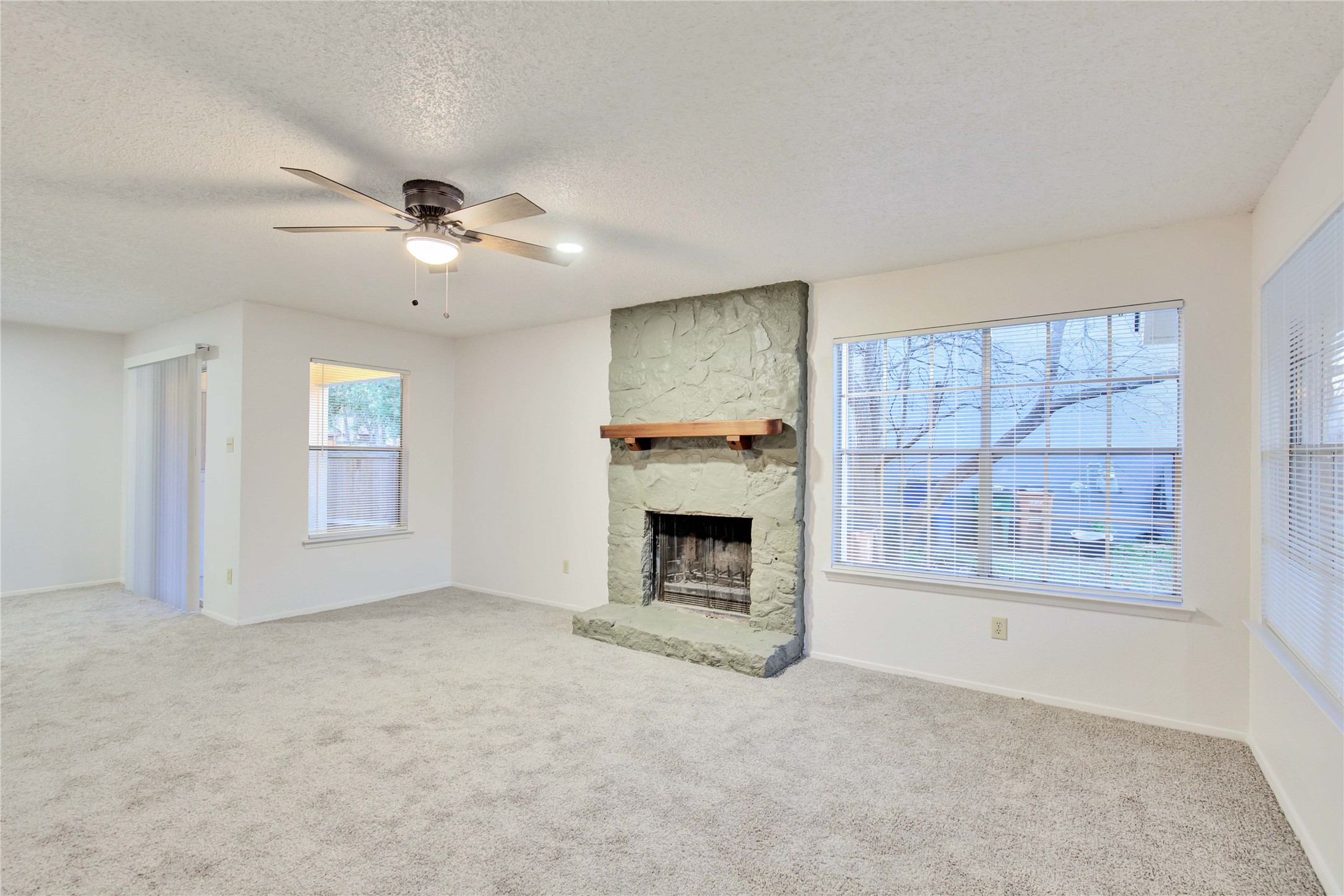2807 Firecrest Drive Austin, TX 78748 - Photo 17 of 30 Living area featuring a stone fireplace with a wood mantel, light gray carpet, and multiple windows