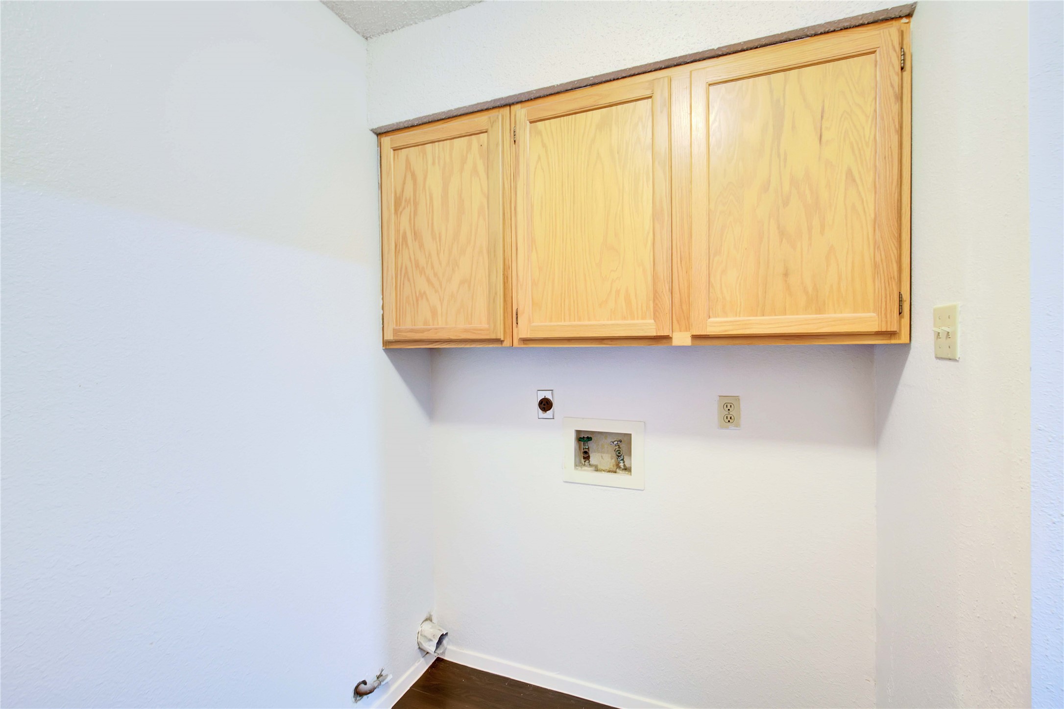2807 Firecrest Drive Austin, TX 78748 - Photo 5 of 30 Laundry area featuring three wood-finish upper cabinets with a countertop, white textured walls, wood-finish flooring, and essential utility hookups