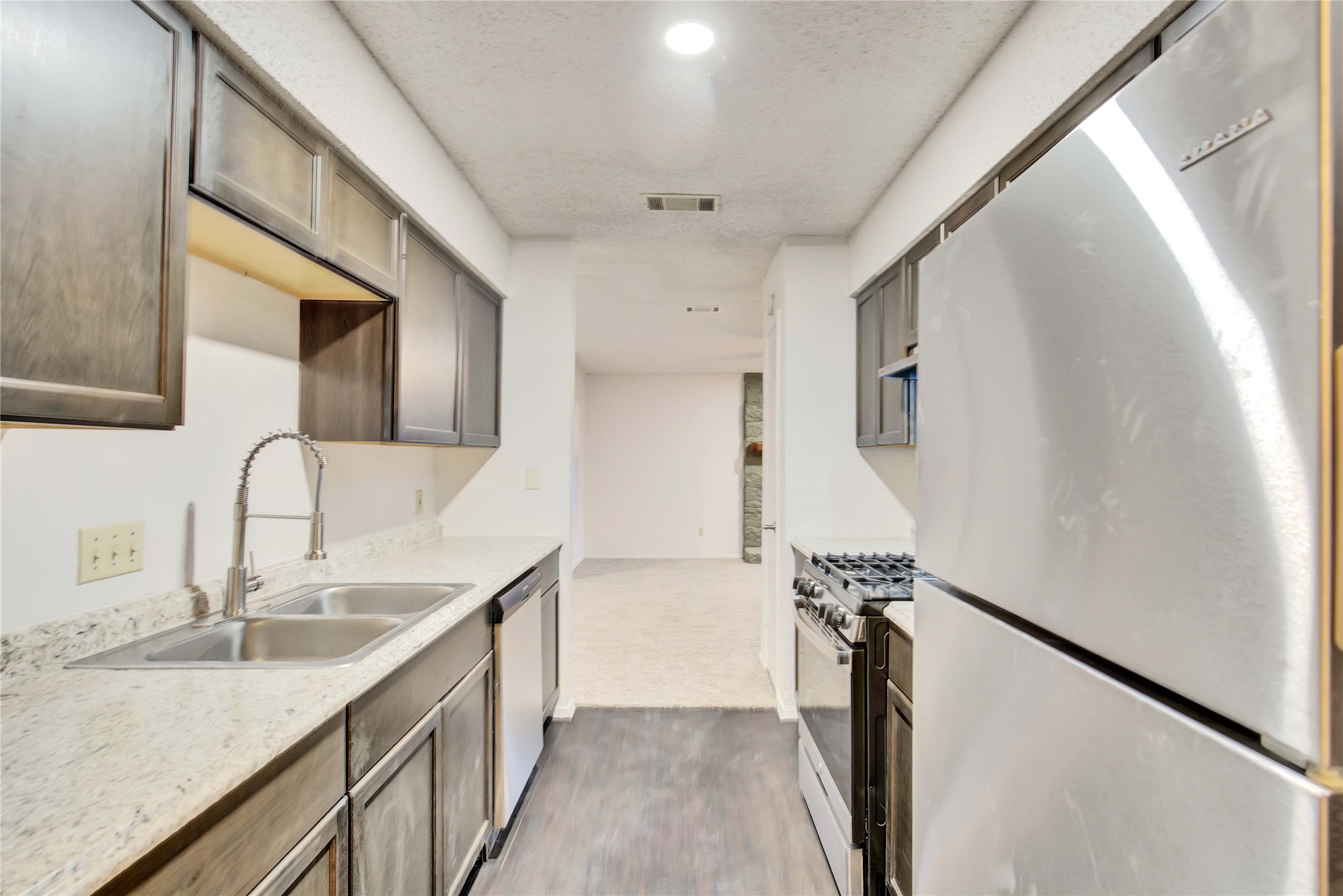 2807 Firecrest Drive Austin, TX 78748 - Photo 6 of 30 Galley kitchen featuring wood-finish cabinetry, light-toned countertops, a dual-basin stainless steel sink with a high-arc faucet, and stainless steel appliances