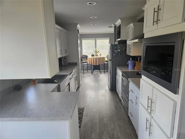 a kitchen with stainless steel appliances granite countertop a stove a refrigerator a sink a dining table and chairs with wooden floor