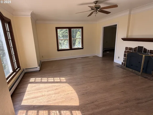 a view of a livingroom with a fireplace a ceiling fan and wooden floor