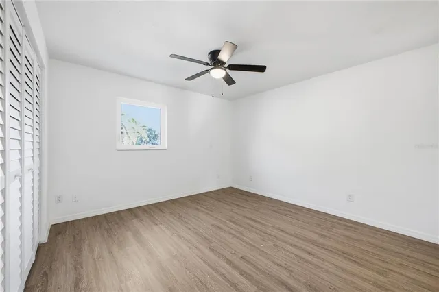 an empty room with wooden floor ceiling fan and windows