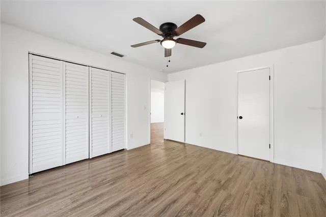 an empty room with wooden floor chandelier fan and windows