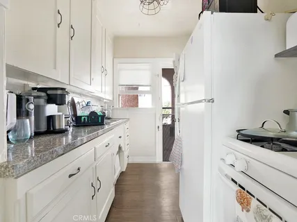 a kitchen with granite countertop a refrigerator a sink and white cabinets