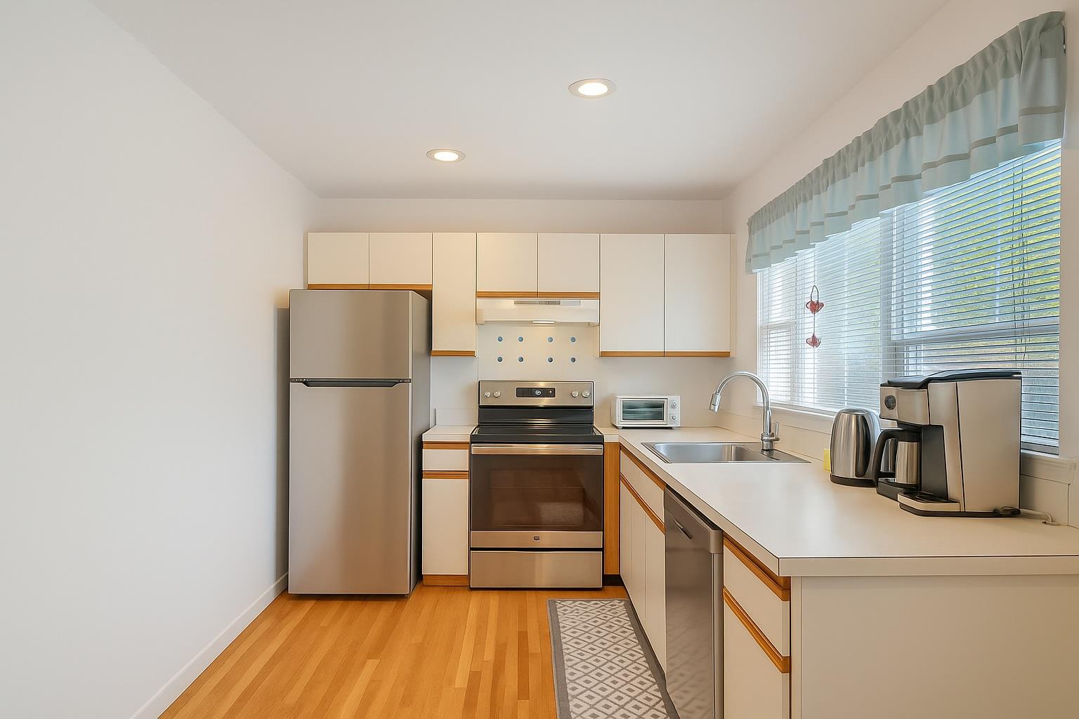 28 Huntting Road East Hampton, NY 11937 - Photo 3 of 14 Kitchen featuring appliances with stainless steel finishes, a sink, under cabinet range hood, light wood-style floors, and light countertops