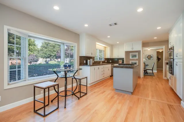 a kitchen with stainless steel appliances kitchen island granite countertop a stove a refrigerator a sink a dining table and chairs