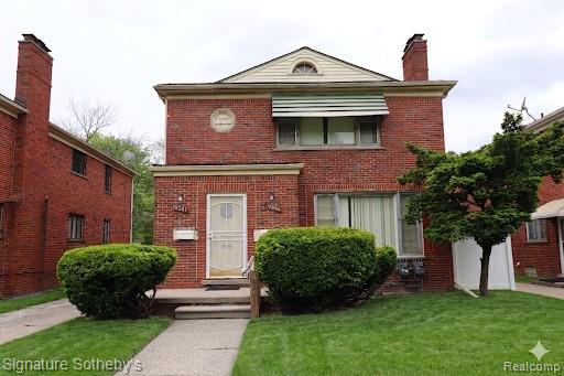 Brick exterior featuring a gabled roofline, decorative window awning, and established front yard landscaping
