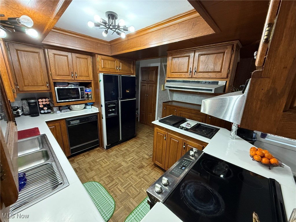 8116 Deer Road Southwest Bowerston, OH 44695 - Photo 16 of 49 Kitchen featuring black appliances, brown cabinetry, light countertops, under cabinet range hood, and ornamental molding