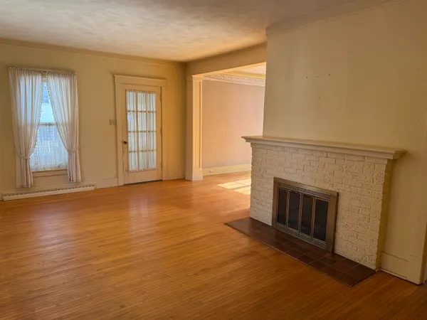 an empty room with wooden floor fireplace and windows