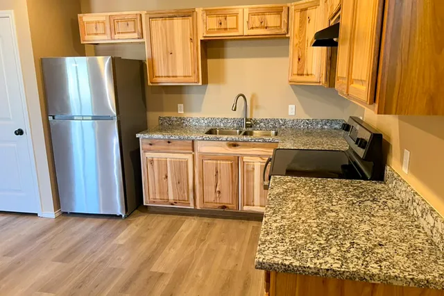 a kitchen with stainless steel appliances granite countertop a refrigerator a stove and a sink with wooden floors