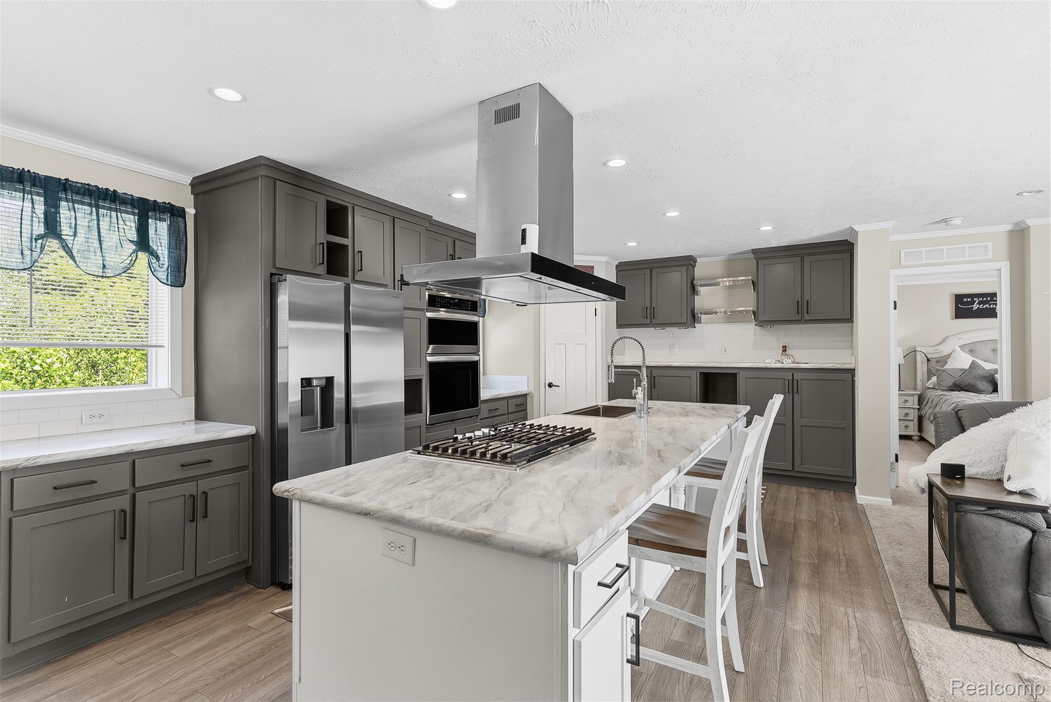 6450 Prince Boulevard Fenton, MI 48430 - Photo 16 of 31 Spacious kitchen featuring an expansive center island with a gas cooktop, sleek stainless steel appliances, ample dark cabinetry, and white countertops complemented by a subway tile backsplash