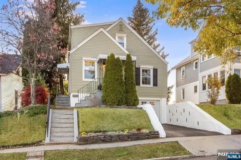 a view of a white house with a yard plants and large tree