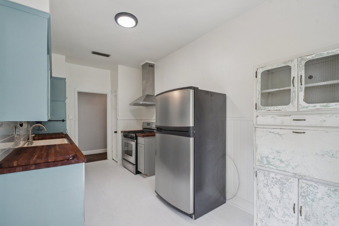 308 Taylor Road Elgin, TX 78621 - Photo 16 of 29 Kitchen with stainless steel appliances, wainscoting, wall chimney exhaust hood, glass insert cabinets, and butcher block counters