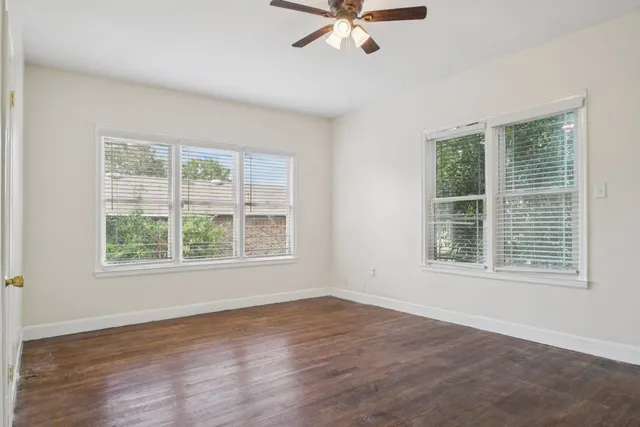 an empty room with wooden floor fan and windows