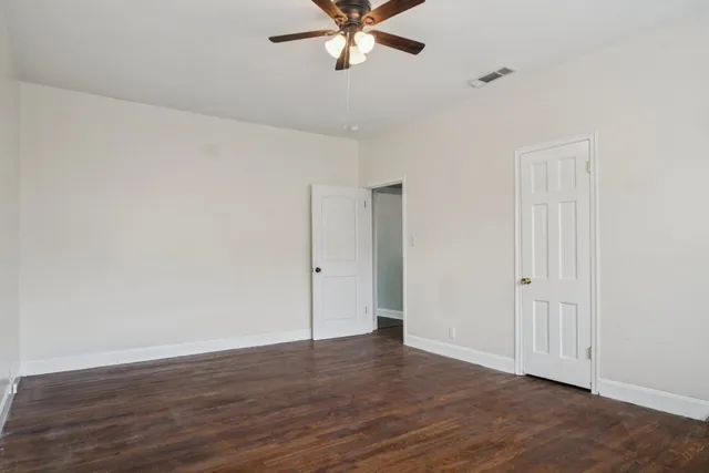 a view of an empty room with wooden floor and a ceiling fan