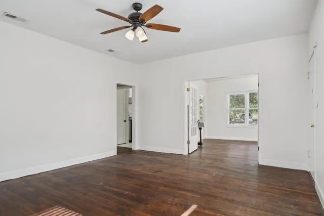 an empty room with wooden floor chandelier fan and windows
