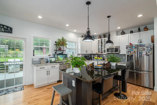 a kitchen with stainless steel appliances kitchen island granite countertop a refrigerator a stove a sink dishwasher a dining table and chairs with wooden floor