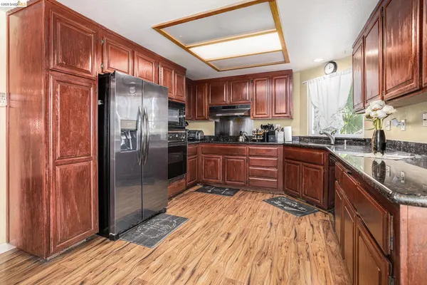 a kitchen with stainless steel appliances granite countertop a refrigerator a sink dishwasher a stove with wooden cabinets and floor