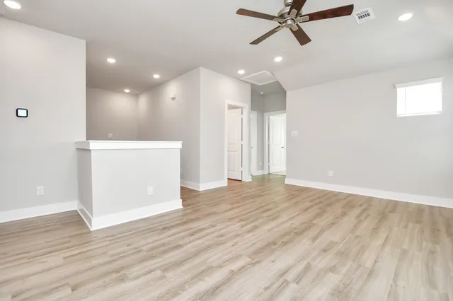 a view of an empty room with wooden floor and a ceiling fan