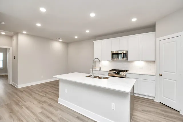 a kitchen with stainless steel appliances a stove a sink cabinets and a wooden floor