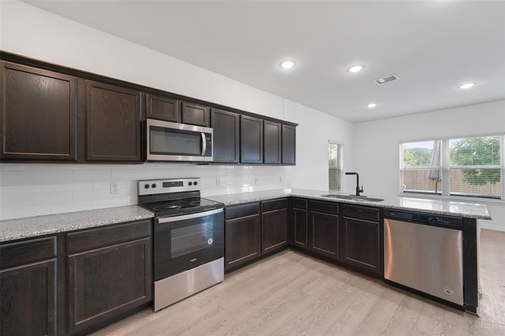 4651 Raleigh Dalton Road Dallas, TX 75227 - Photo 8 of 19 Modern kitchen featuring dark cabinetry with raised-panel doors, stainless steel appliances including a slide-in range and over-the-range microwave, quartz countertops, subway tile backsplash, and light wood-finish flooring
