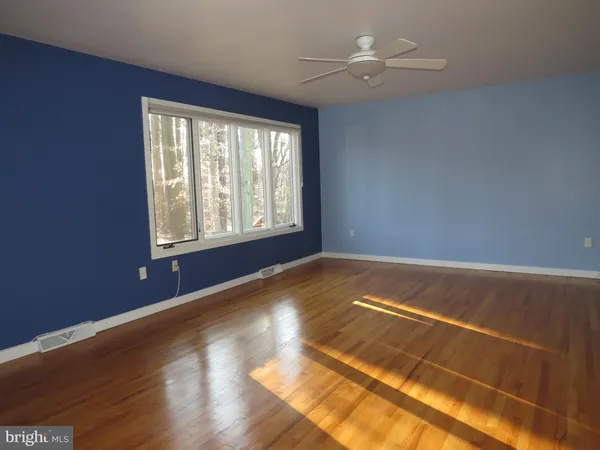 a view of empty room with wooden floor and fan
