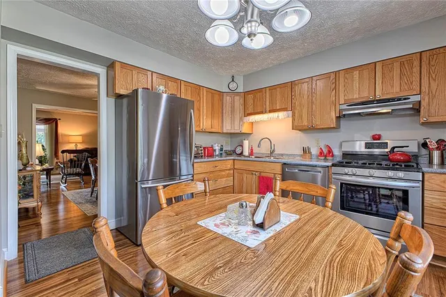 a kitchen with stainless steel appliances granite countertop a refrigerator a stove top oven a sink dishwasher and dining table with wooden floor