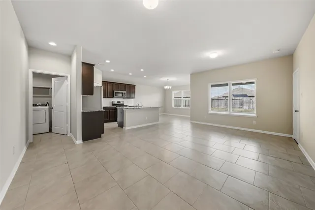 a view of an empty room and a kitchen with windows